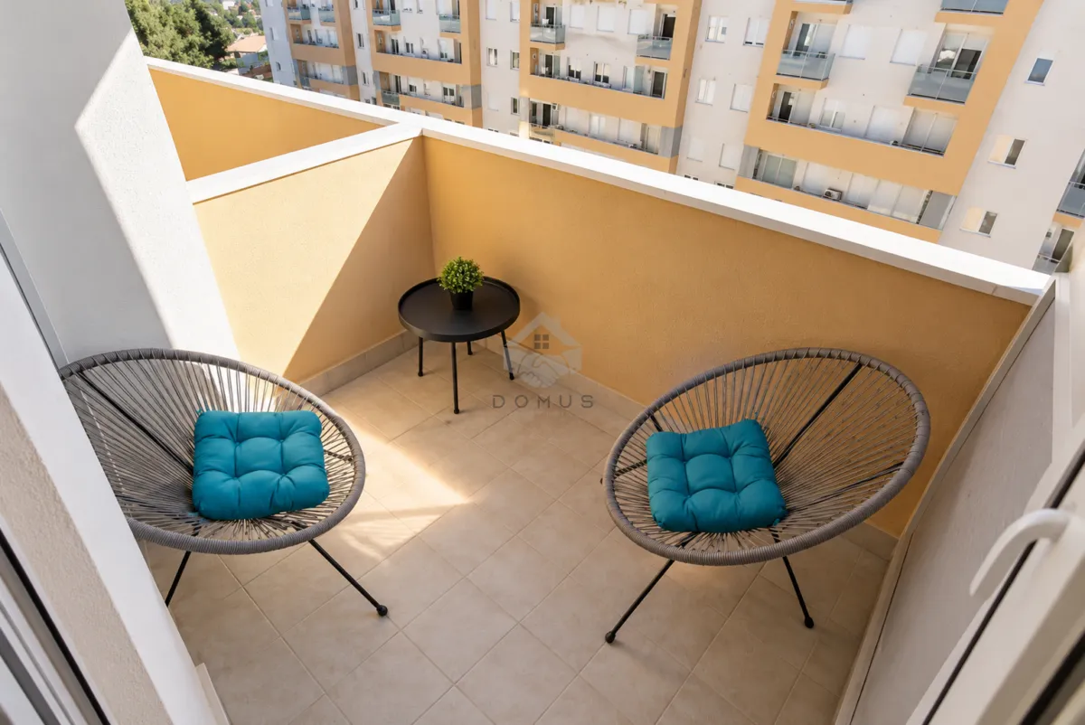 Namtješten balkon sa dvije fotelje, stočićem i pogledom na zgrade.