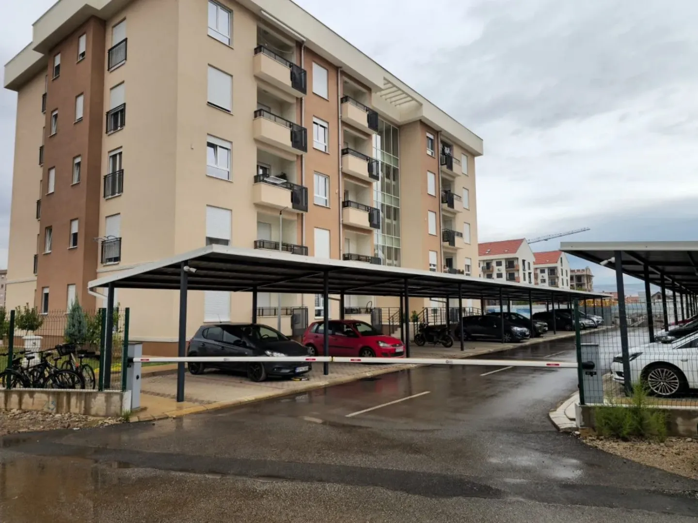 Eksterijer stambene zgrade sa parkingom i natkrivenim prostorom za vozila.