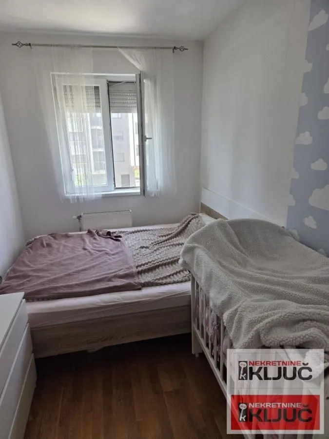Dečija spavaća soba sa krevetom i dečijim krevetcem pored prozora.