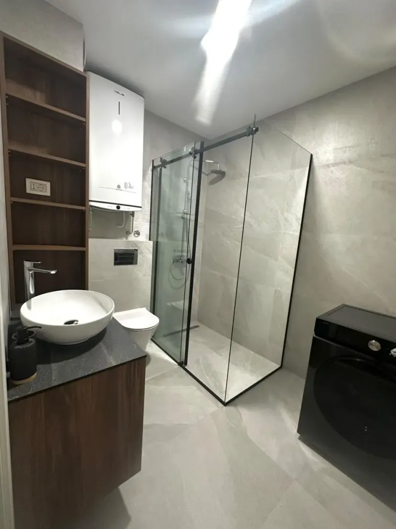 Modern bathroom with a walk-in shower, washbasin, and washing machine.