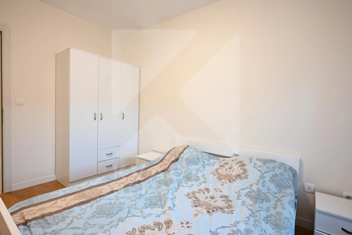 Spavaća soba sa bračnim krevetom, bijelim ormarom i noćnim stočićima.