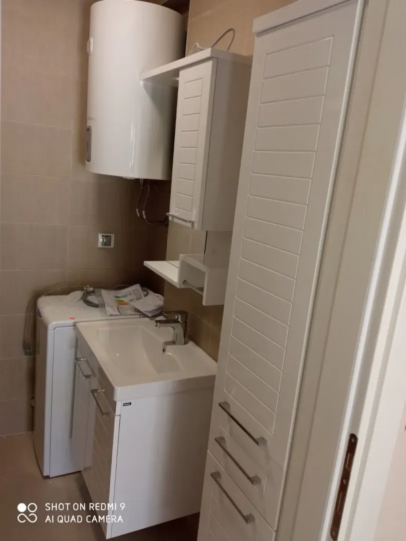 Manje kupatilo sa bijelim namještajem, umivaonikom i bojlerom.