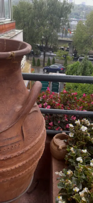 Balkon ukrašen cvećem i velikim zemljanim posudama sa pogledom na zelenilo.