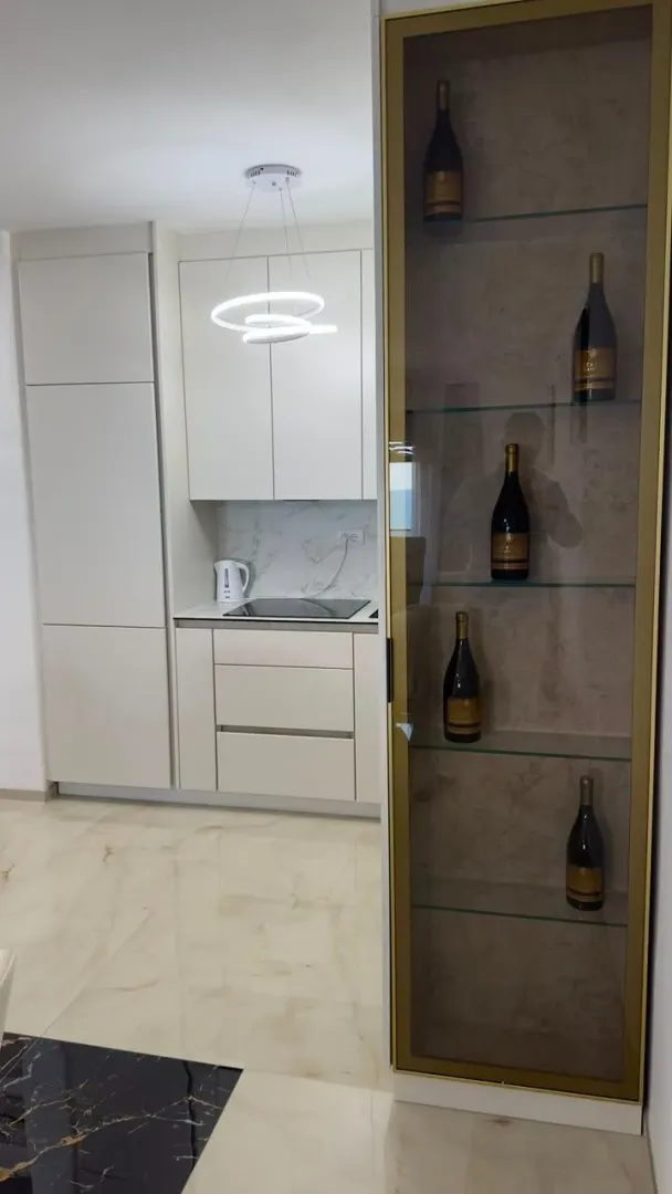 Moderna kuhinja sa bijelim elementima i osvijetljenom vitrinom za vino.