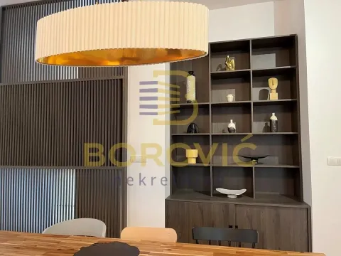 Dining area with a wooden table, shelving unit, and a modern chandelier. - image 5