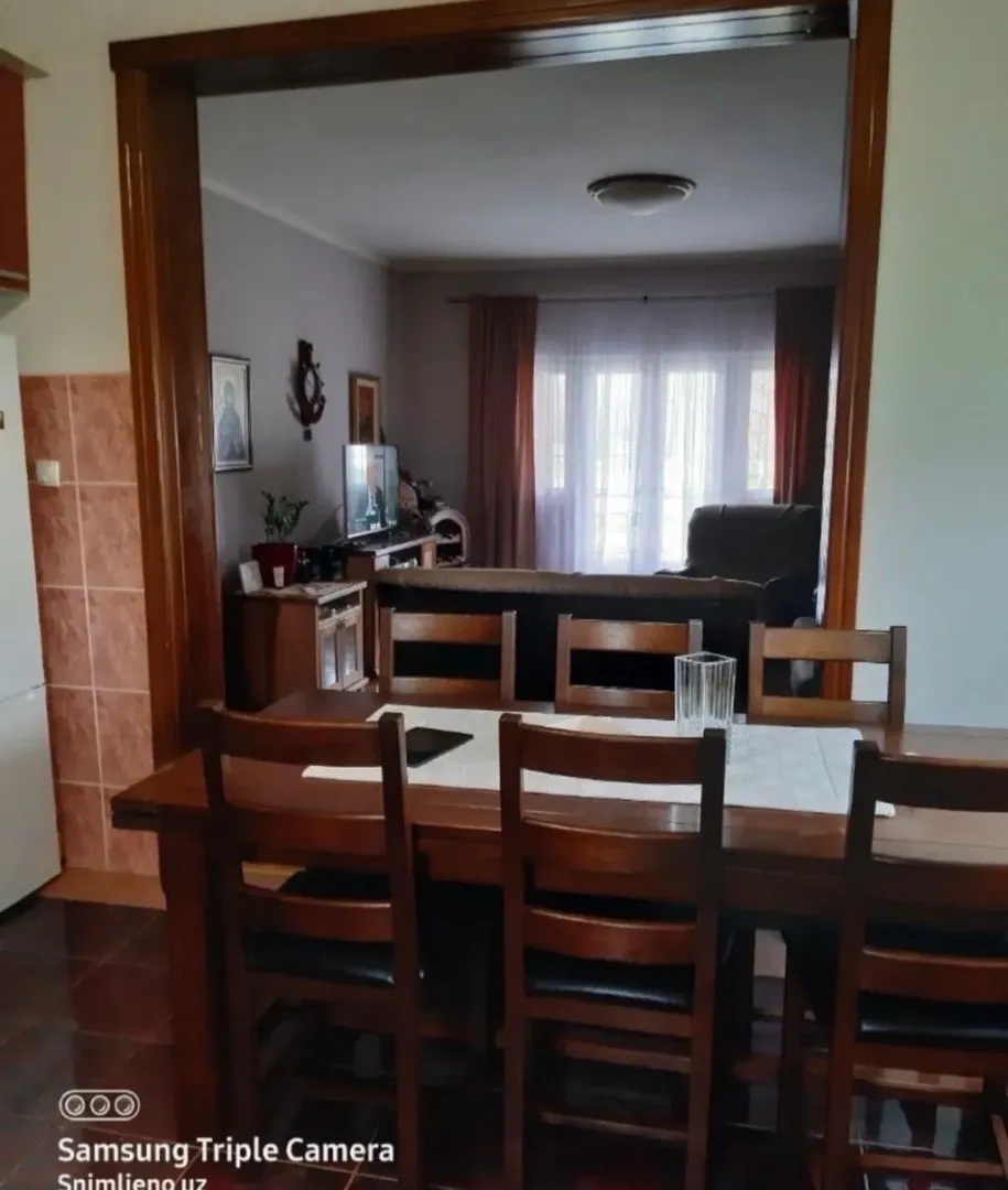 Trpezarija sa velikim drvenim stolom i stolicama, sa pogledom na dnevnu sobu.