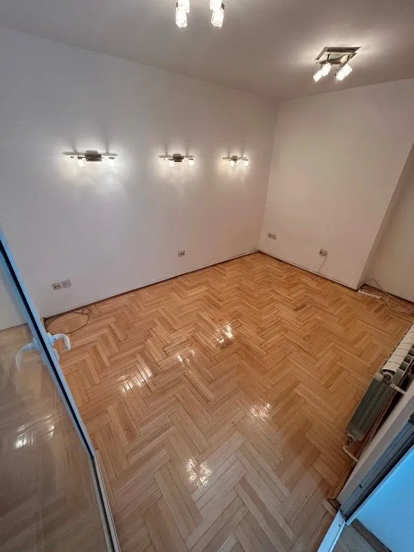Prazna prostorija sa parketom i rasvetom na zidovima.