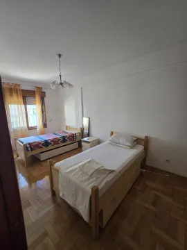 Spavaća soba sa dva drvena kreveta, parketom i prozorom sa žutim zavesama. - image 13