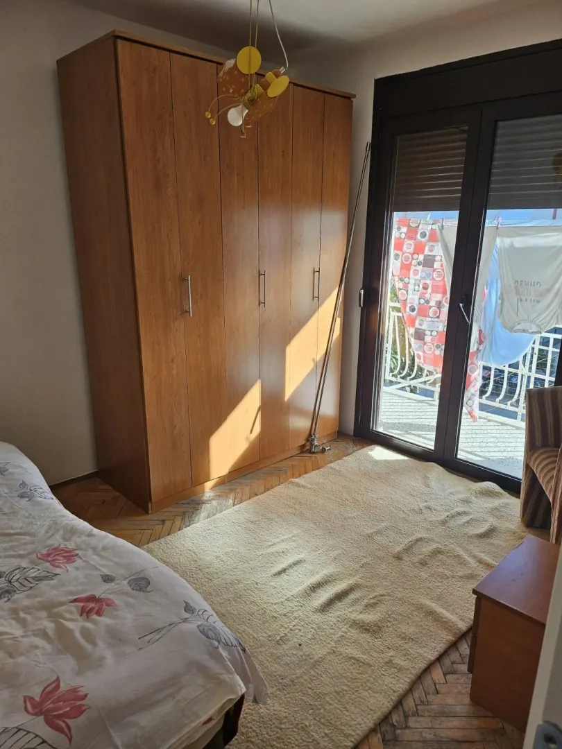 Spavaća soba sa velikim drvenim ormarom i izlazom na balkon.