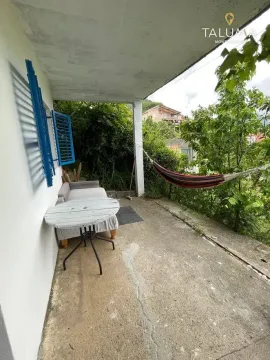 Natkrivena terasa sa stolom, sofom i ležaljkom okružena zelenilom. - image 10