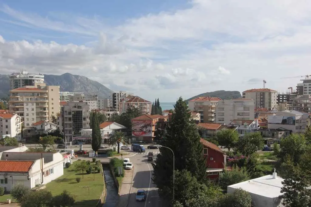 Pogled sa visine na gradsko naselje, planine i more u pozadini.
