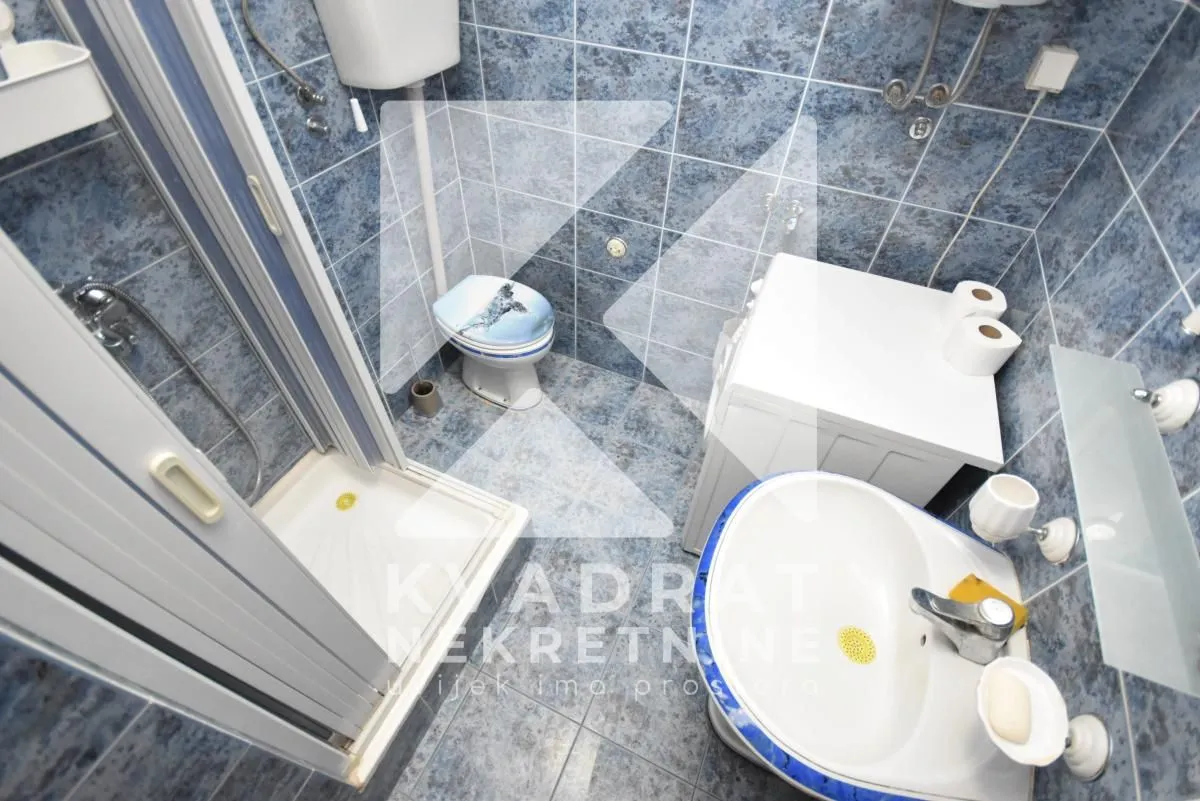 Smaller tiled bathroom equipped with a shower cabin, sink, and toilet.