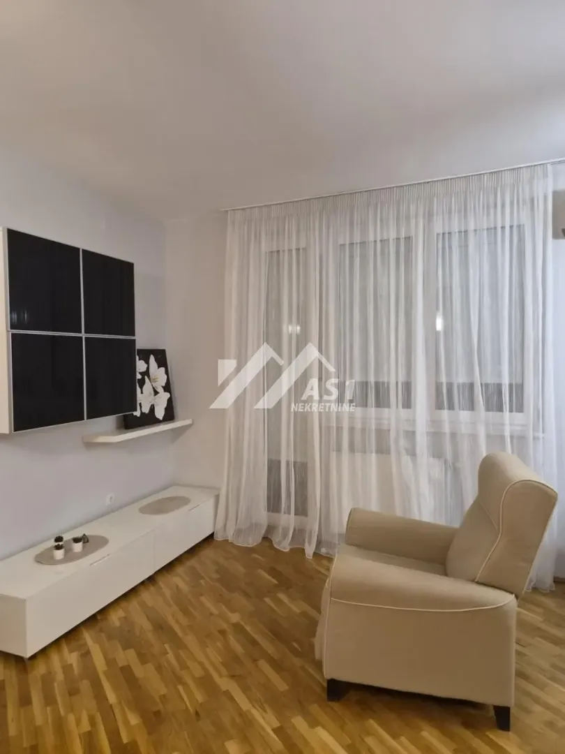 Dnevna soba sa udobnom foteljom i TV komodom.