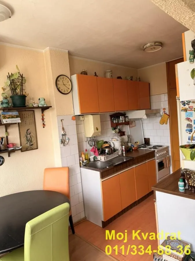 Manja kuhinja sa narandžastim elementima i trpezarijskim stolom u uglu.