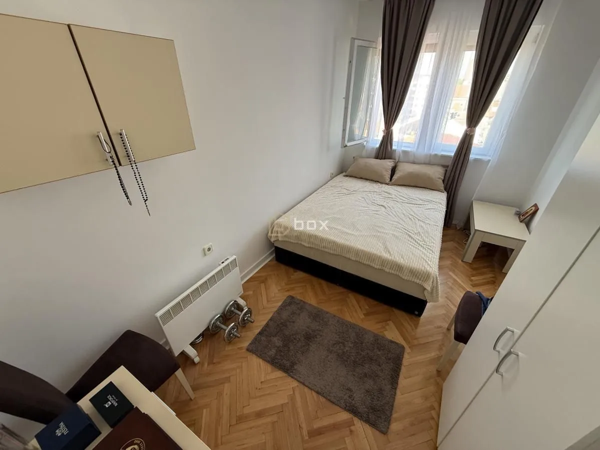 Nameštena spavaća soba sa bračnim krevetom, radnim stolom i parketom.