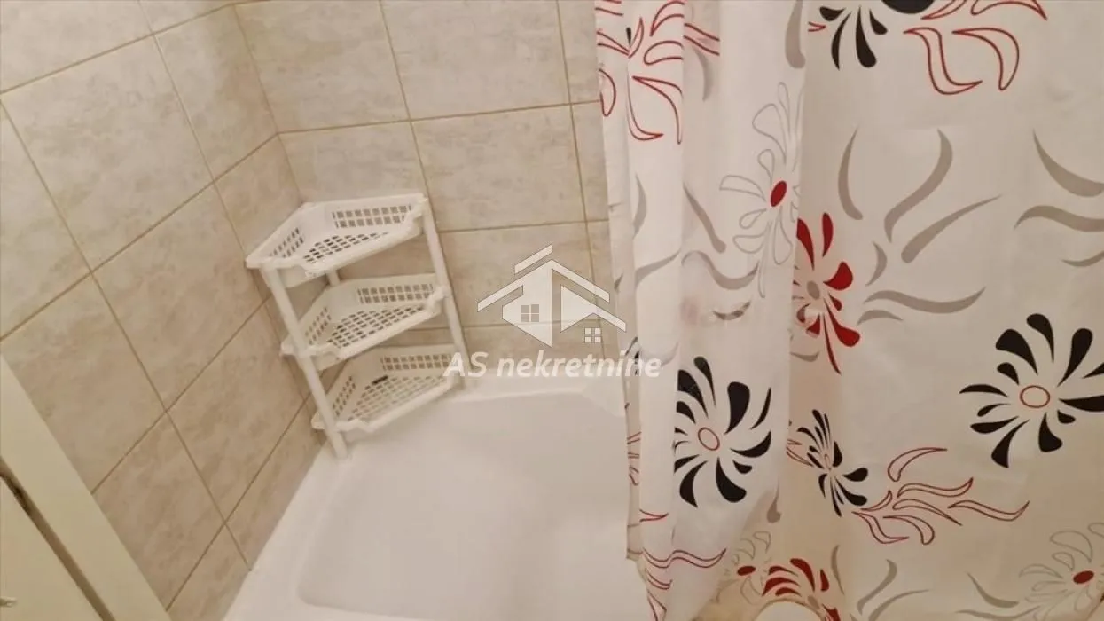 View of the bathtub with a curtain and shelves in the bathroom.
