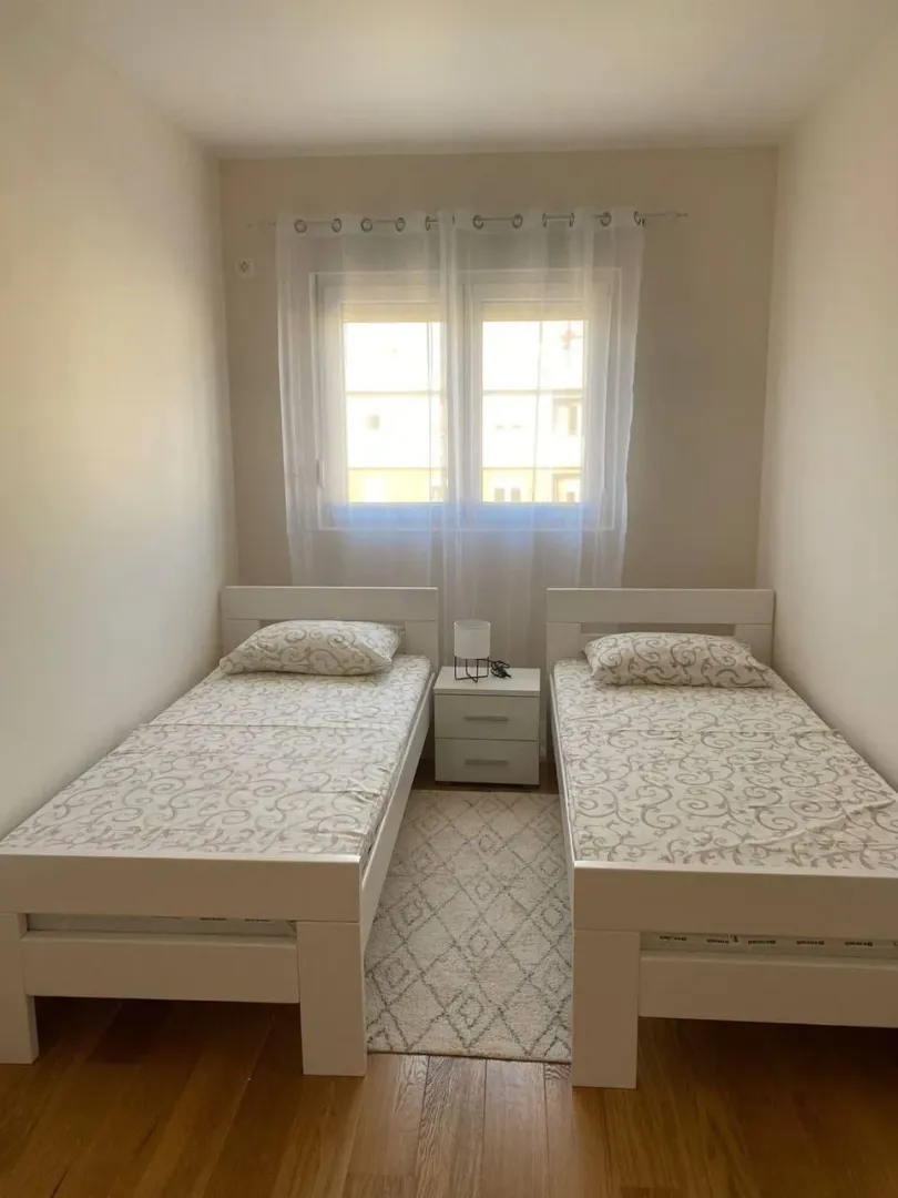 Spavaća soba sa dva odvojena kreveta, noćnim stočićem i prozorom.