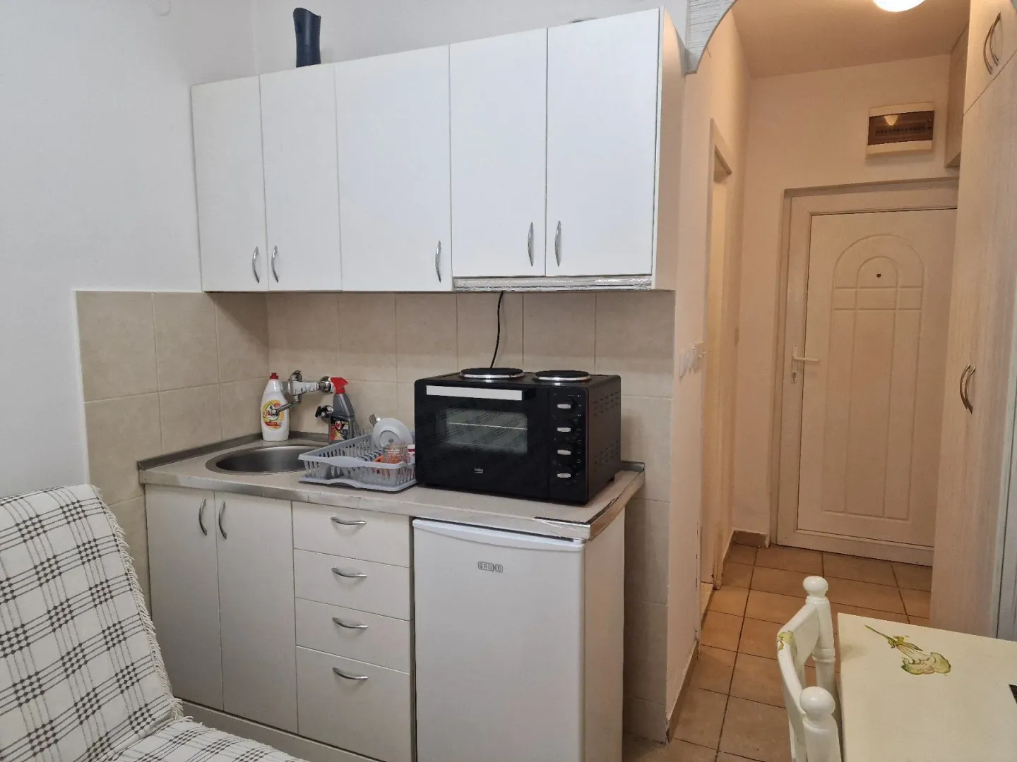 Small kitchen with white units, sink, and mini cooker.