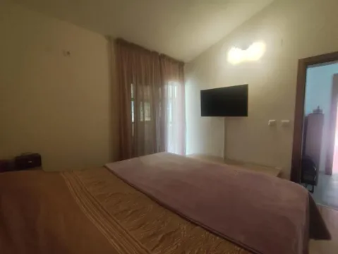 Spavaća soba sa bračnim krevetom, televizorom na zidu i balkonskim vratima sa zavesama. - image 12