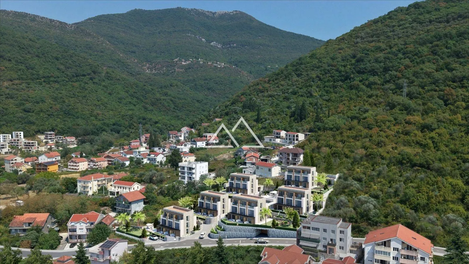 Pogled iz vazduha na novo naselje u izgradnji okruženo šumom i brdima.