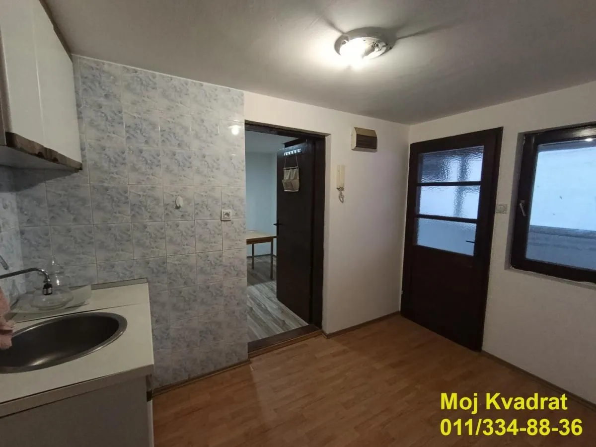 Small kitchen with a sink, wall tiles, and a door leading to another room.