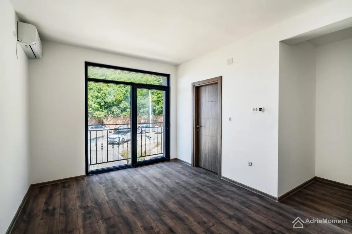 Empty room with dark parquet flooring, balcony doors, and an air conditioning unit.