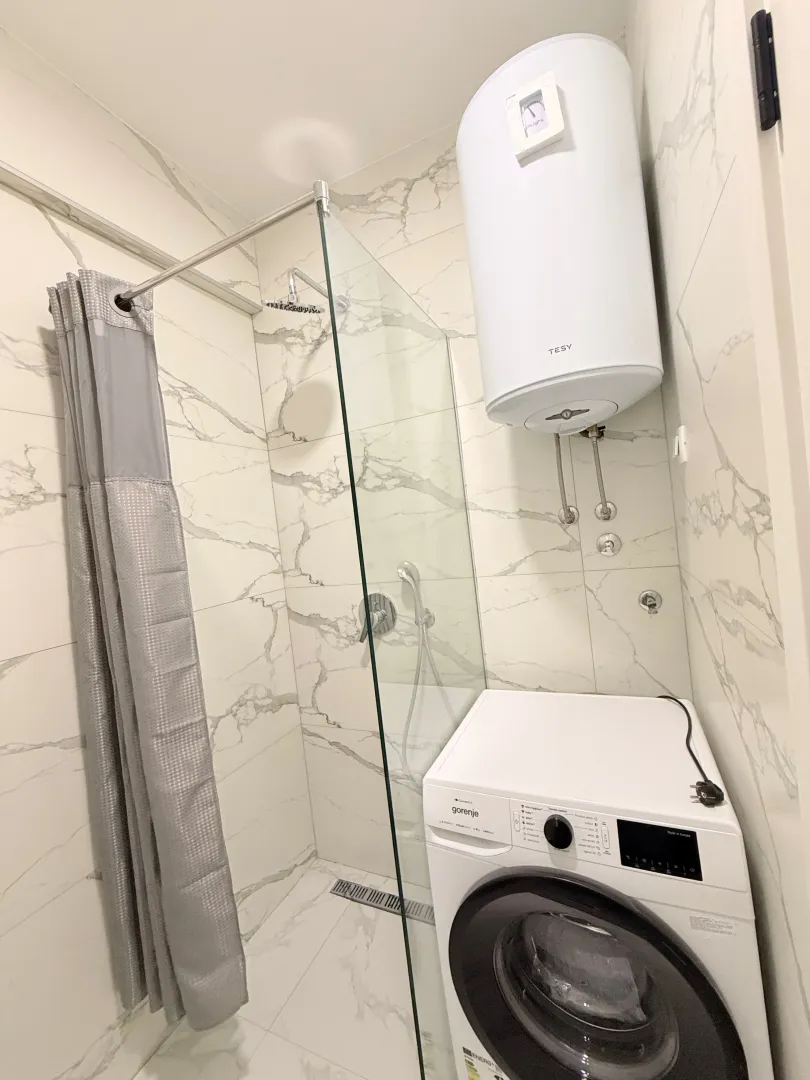 Manje kupatilo sa tuš kabinom, bojlerom i veš mašinom.