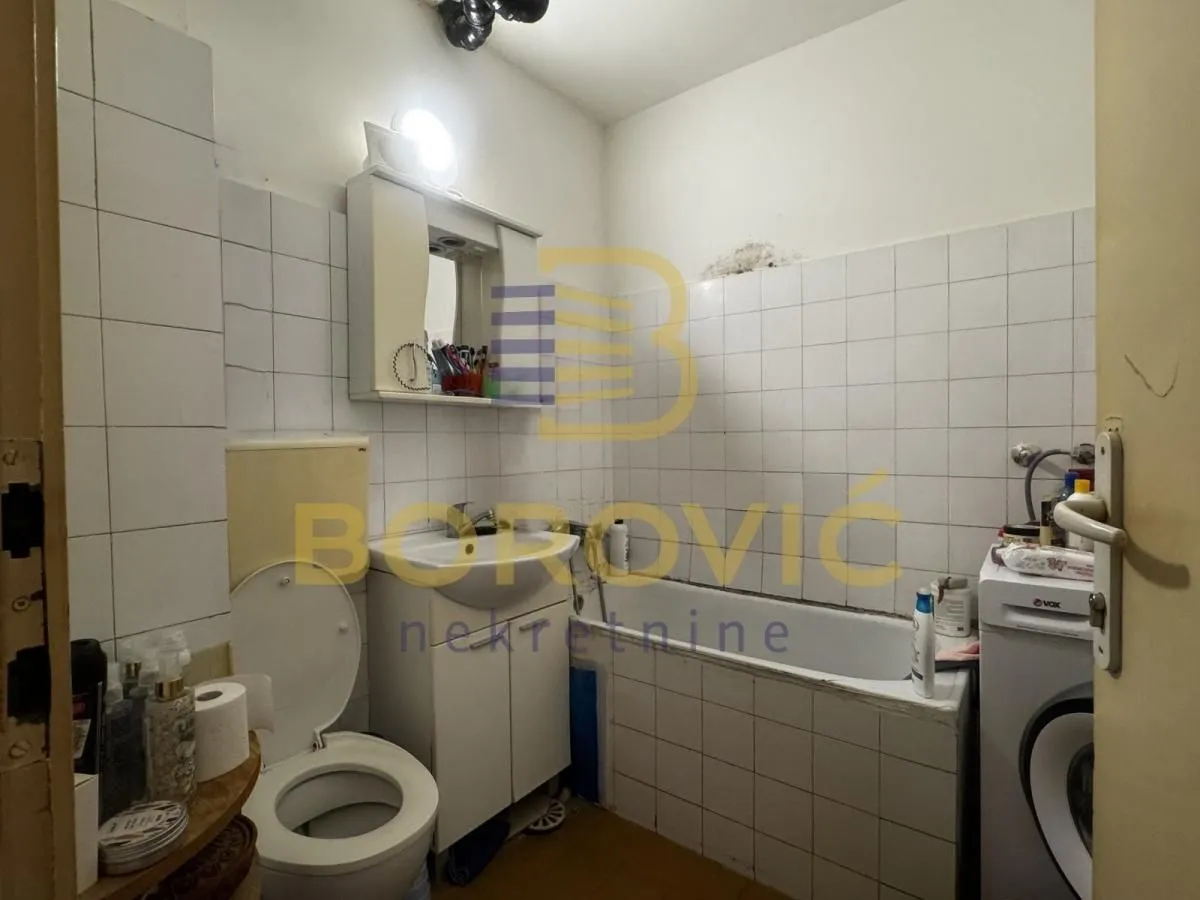 Manje kupatilo sa kadom, toaletom i umivaonikom obloženo belim pločicama.