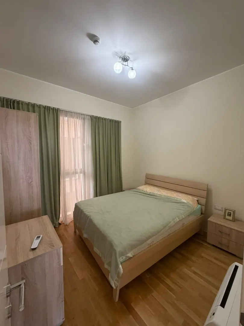 Furnished bedroom with a double bed, wardrobe, and a window with green curtains.