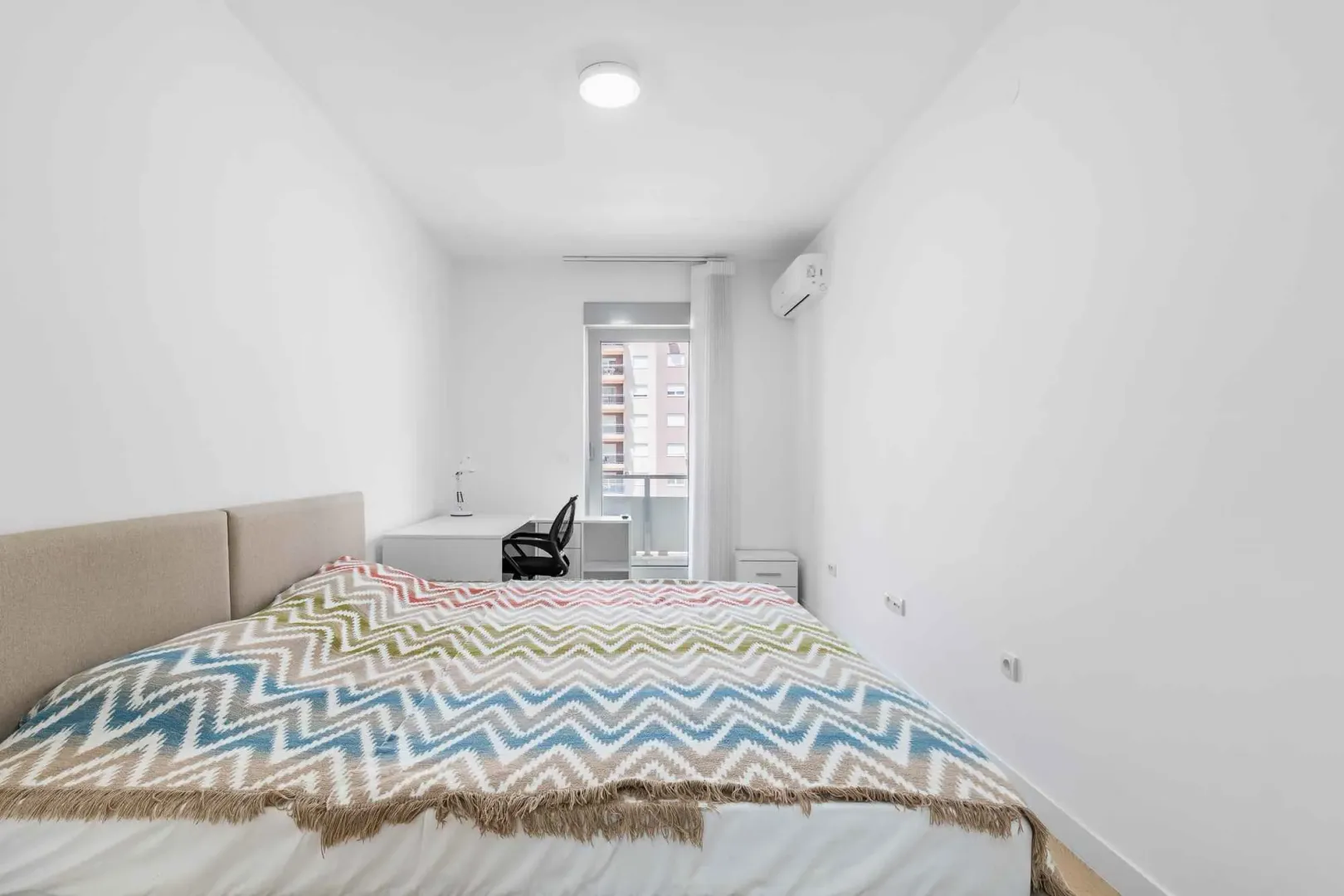 Bright bedroom with a bed, desk, and balcony access.