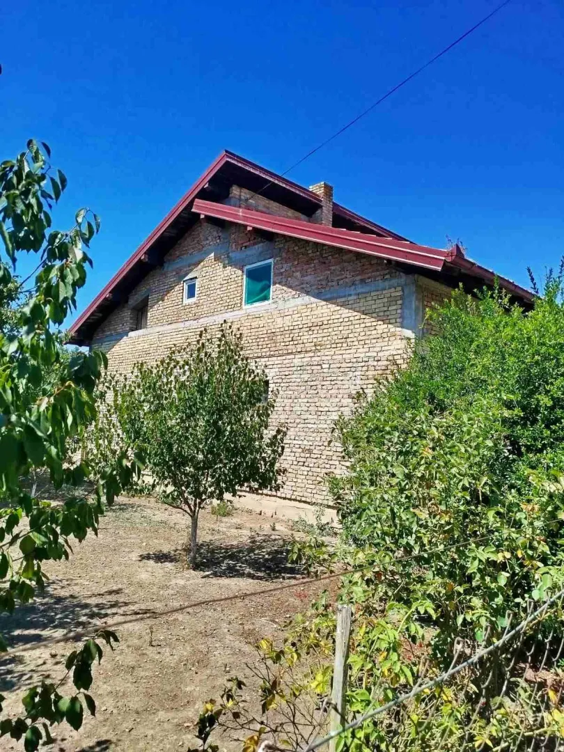 Pogled na spoljašnjost kuće u izgradnji sa dvorištem i rastinjem.