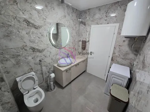 Modern bathroom equipped with marble tiles, a washbasin, toilet, and washing machine. - image 12