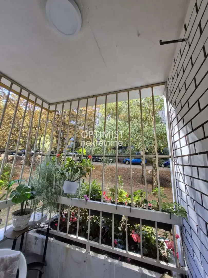 Natkriveni balkon sa zaštitnom ogradom i saksijama sa cvećem.