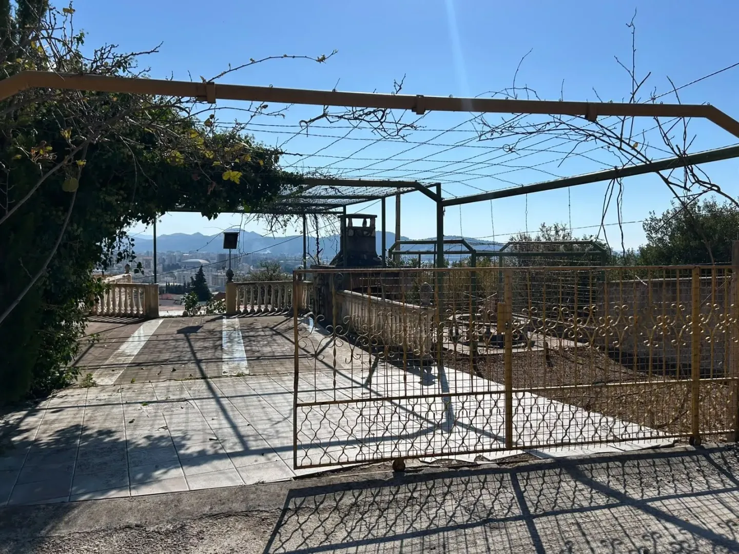Popločano dvorište sa metalnom kapijom i pogledom na grad.
