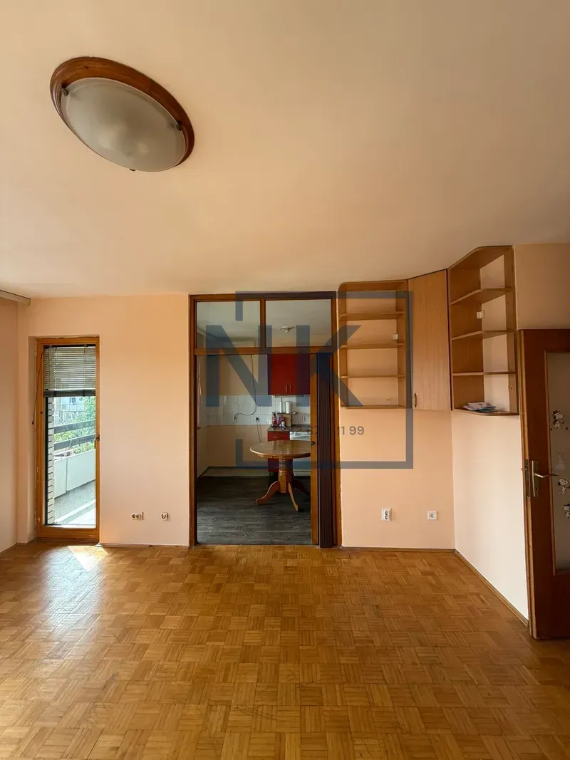 Empty living room with parquet flooring and a view of the kitchen.