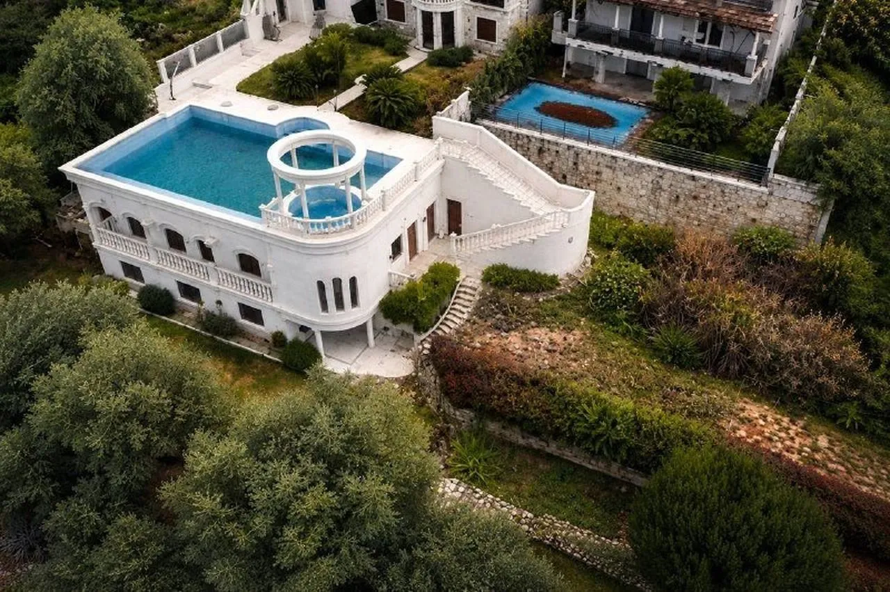 Aerial view of a white house with a rooftop pool and a garden surrounded by greenery.