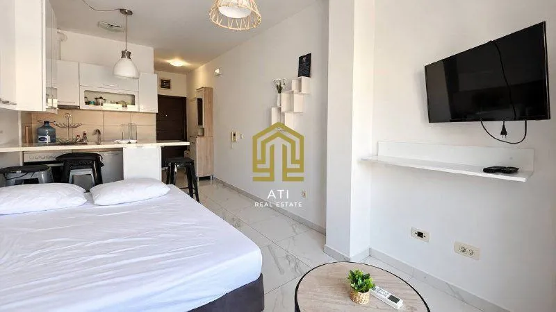 Studio apartment with a bed, kitchen, and wall-mounted TV.