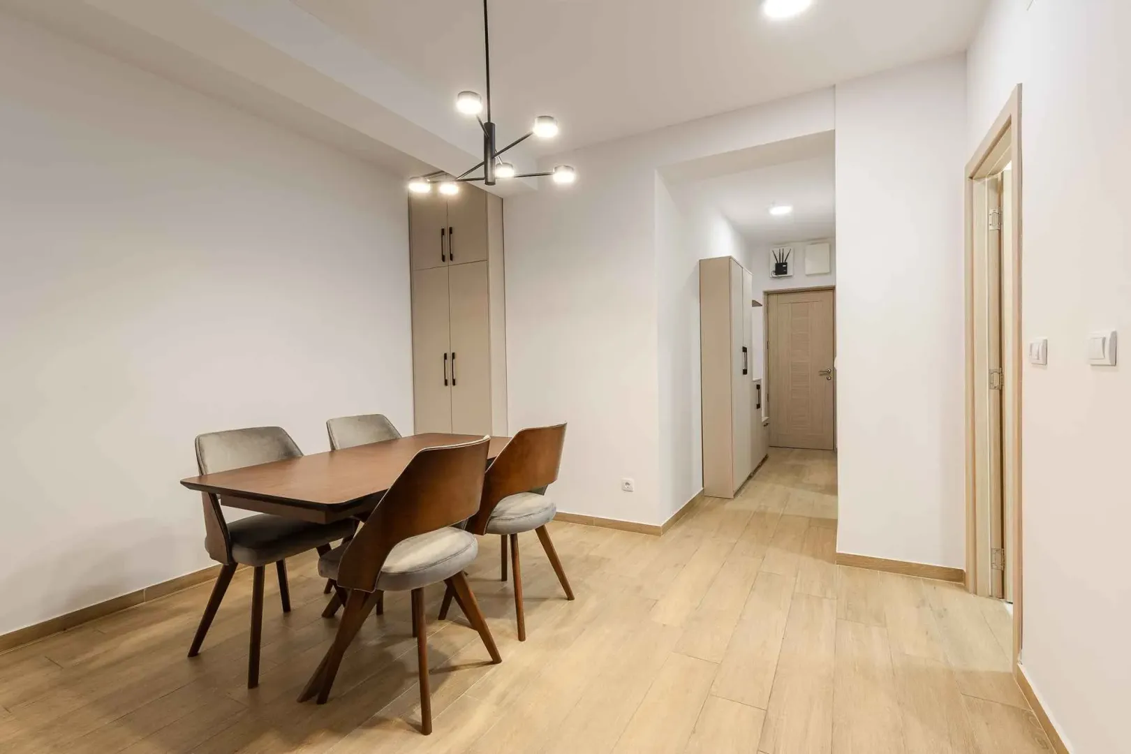 Trpezarija sa drvenim stolom, stolicama i lusterom u modernom stanu.