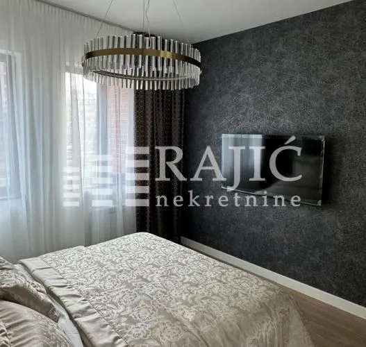 Furnished bedroom with a double bed, modern chandelier, and dark feature wall.