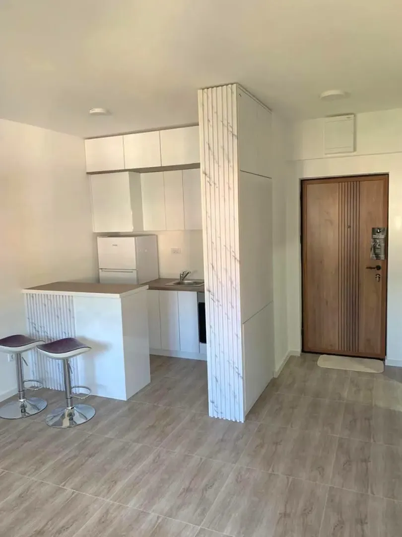 Small white kitchen with a breakfast bar and bar stools inside the apartment.