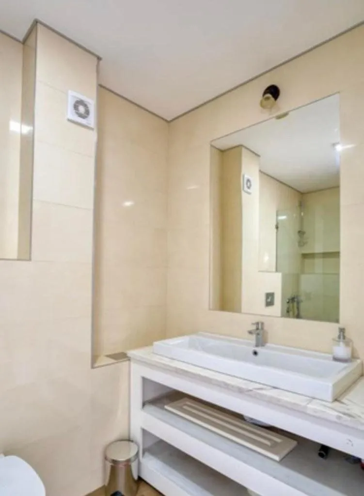 Bathroom with a washbasin, large mirror, and light-toned tiles.