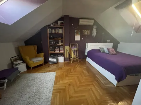 Potkrovlje opremljeno kao spavaća soba sa bračnim krevetom, žutom foteljom i policama za knjige. - image 11