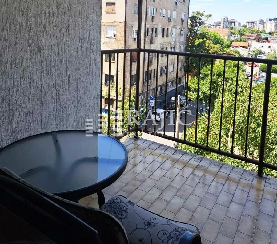 Small furnished balcony with a table and a view of surrounding buildings and the street.