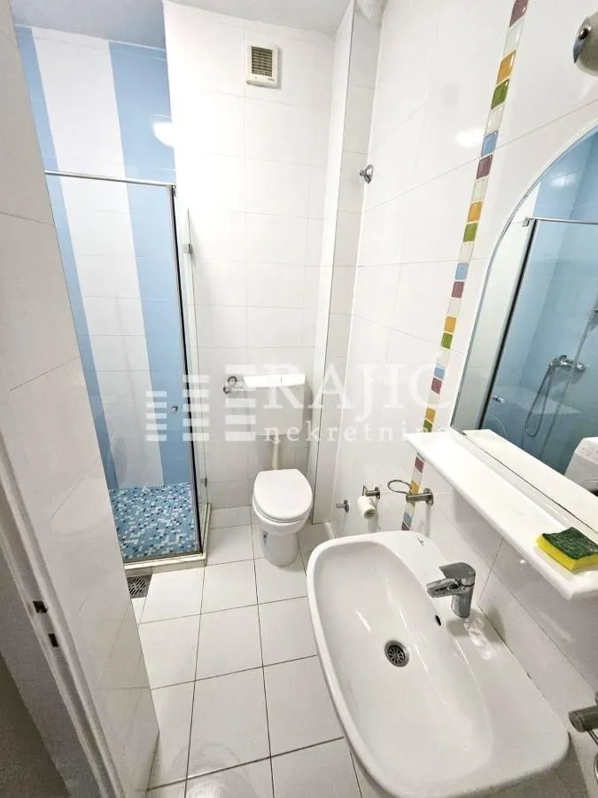 View of a bright bathroom with a shower cabin, washbasin, and toilet.