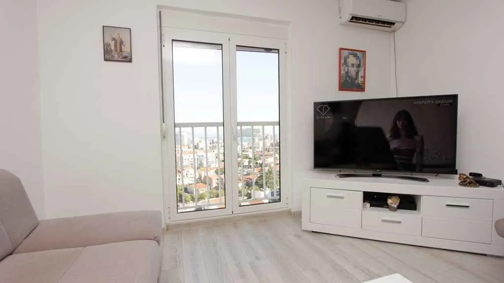 Svijetla dnevna soba sa izlazom na balkon i pogledom na grad.