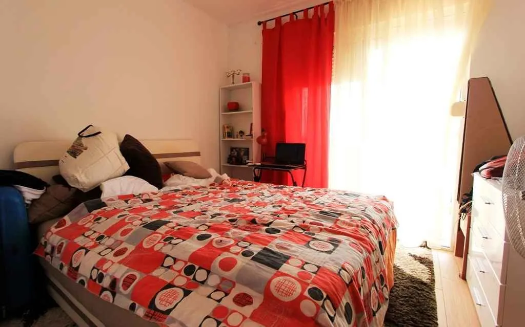 Svijetla spavaća soba sa bračnim krevetom i crvenim zavjesama.