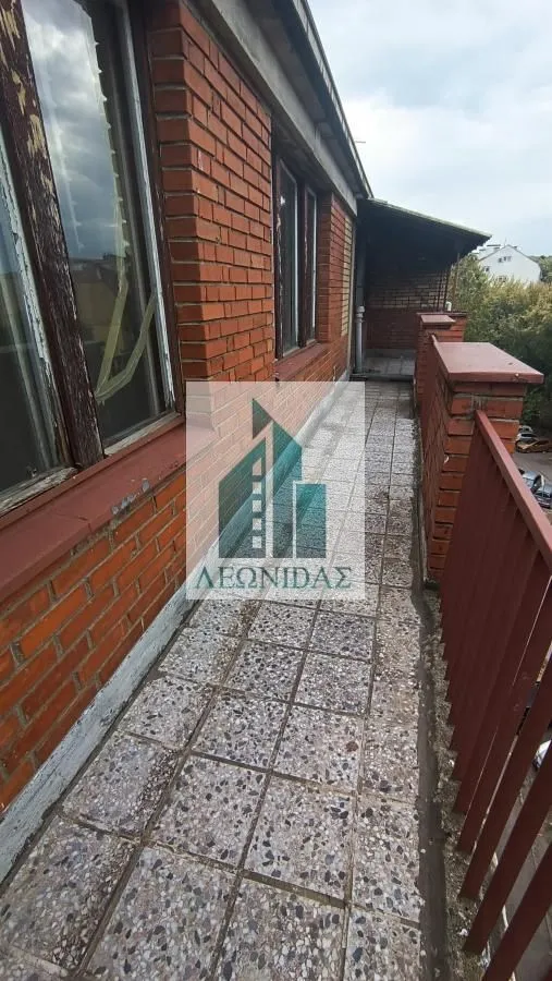 Dugačak popločani balkon sa ciglenom ogradom i pogledom.