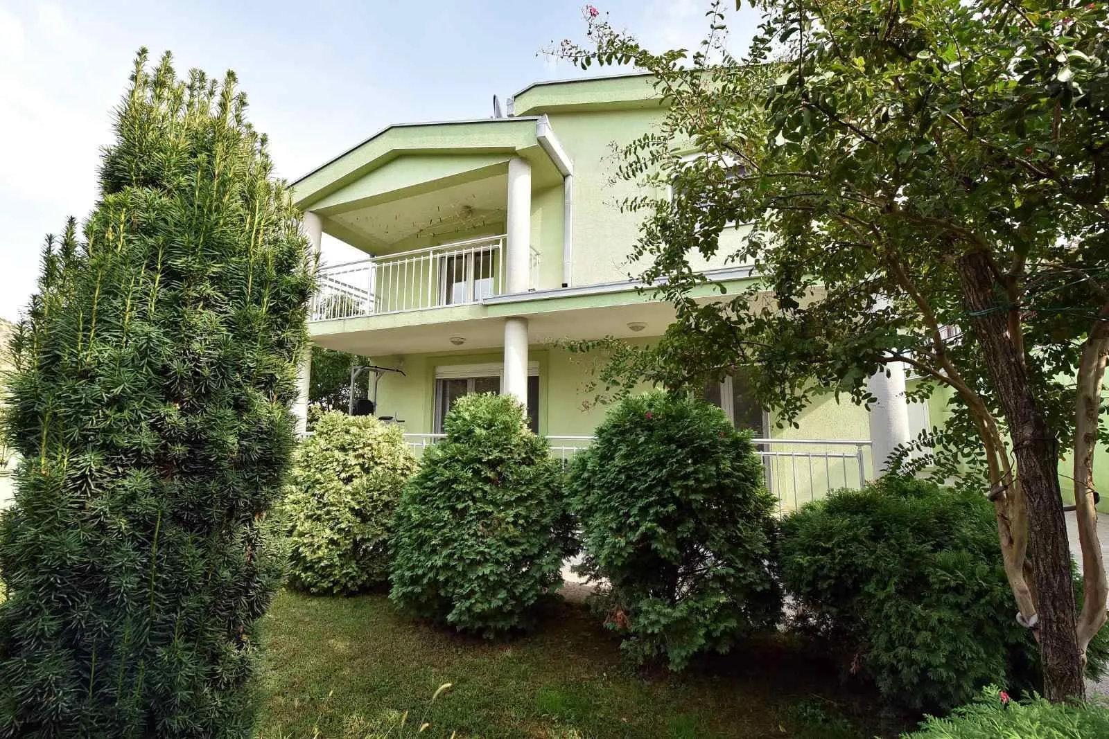 View of the courtyard and facade of a two-story house with landscaped greenery.