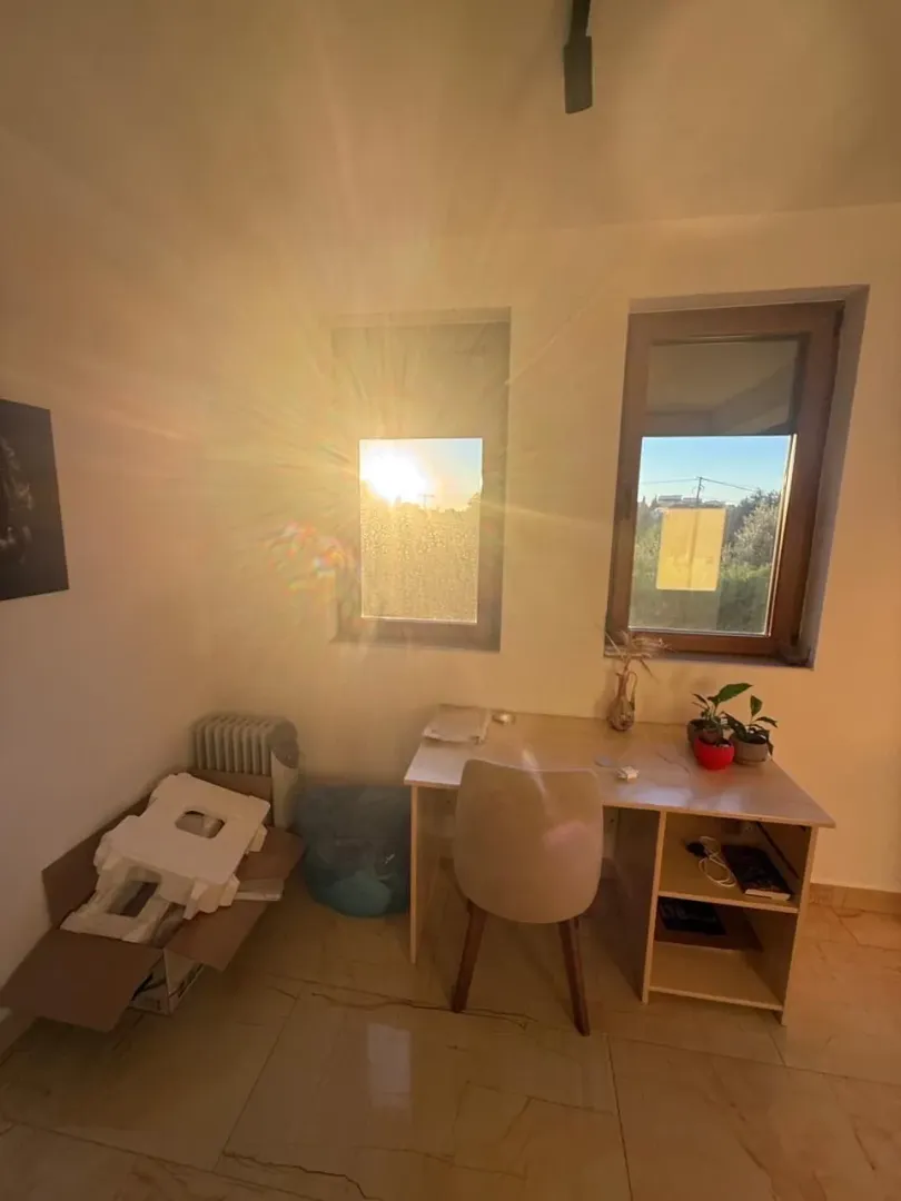 Manja soba sa radnim stolom i prozorom kroz koji sija sunce.