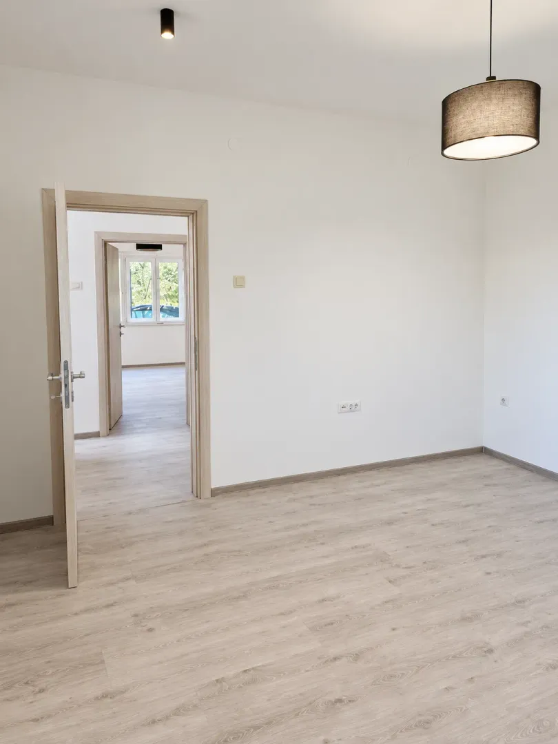 Empty room with light laminate flooring and open doors leading to other rooms.